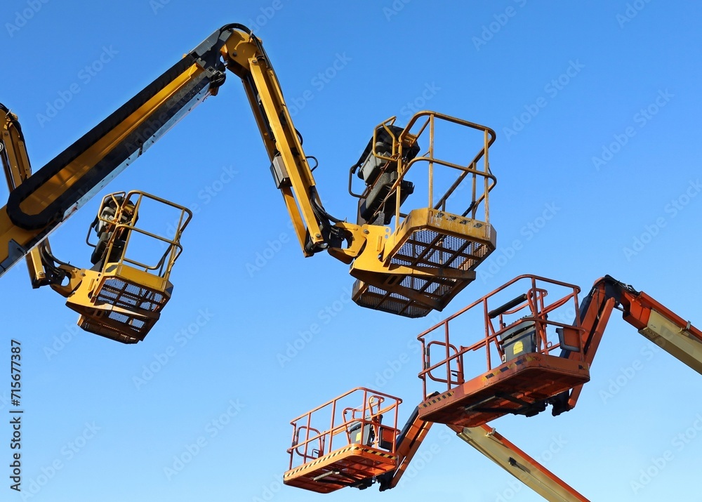Fototapeta premium Two aerial working platforms of cherry pickers in front of other two. Blue sky background.