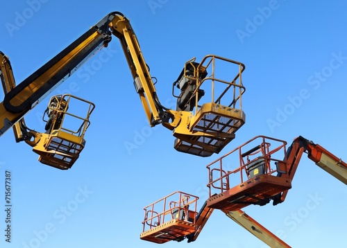 Two aerial working platforms of cherry pickers in front of other two. Blue sky background.