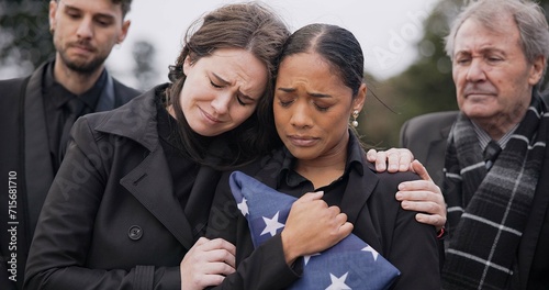 Funeral, death and support for a woman with a flag at a cemetery in mourning at a memorial service. Sad, usa and an army wife as a widow in a graveyard feeling the pain of loss or grief with a friend photo