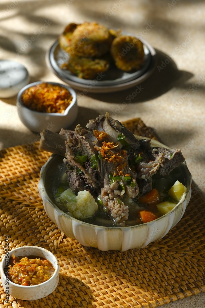 A bowl of beef rib soup on rattan placemat. Delicious food for lunch. Sop daging A bowl of beef rib soup on rattan placemat. Delicious food for lunch. Sop daging