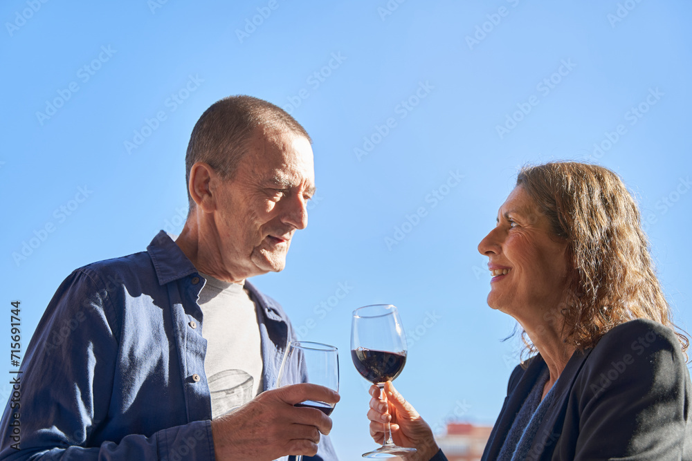 Mature married couple at drinking a glass of wine at patio over blue sky with copy space Mature married couple at drinking a glass of wine at patio over blue sky with copy space