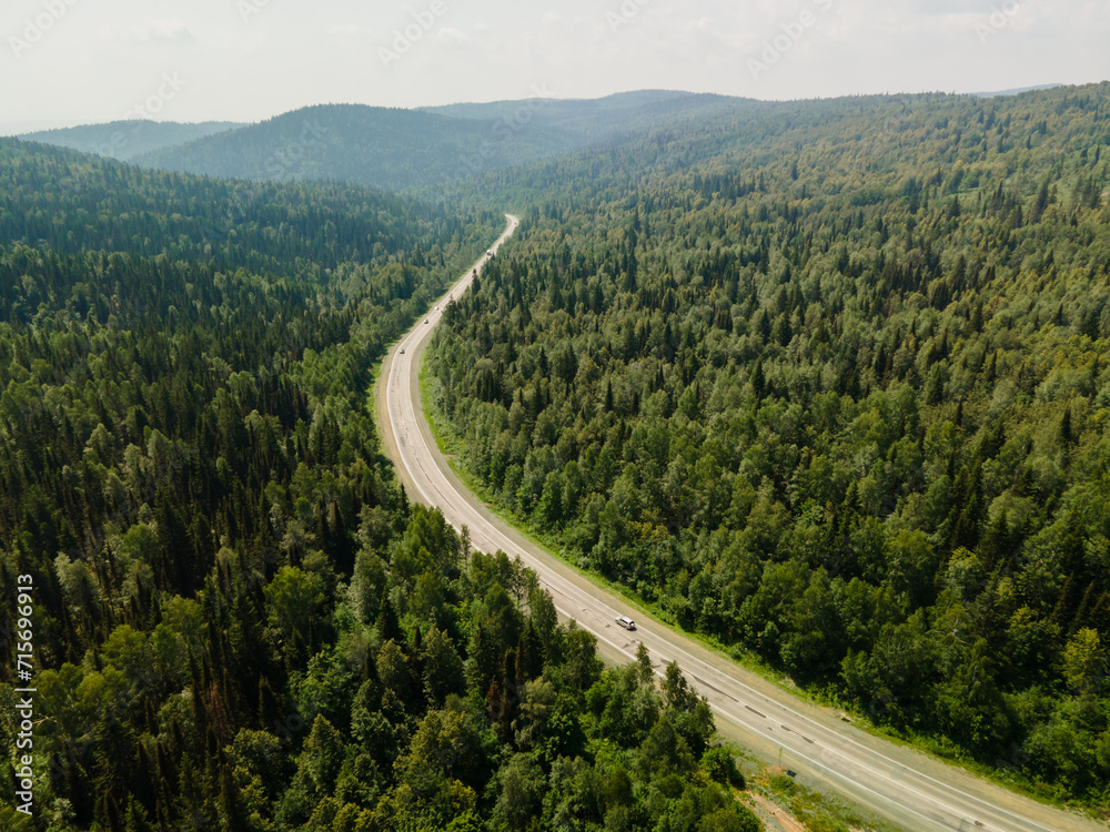 Aerial top view asphalt road in a pine green forest against a blue sky background on a sunny day. Mountains, Nature Reserve, ecopark. Nature background. Photo from the drone.