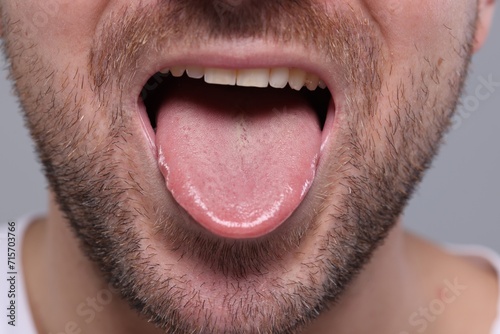 Closeup view of man showing his tongue on grey background photo