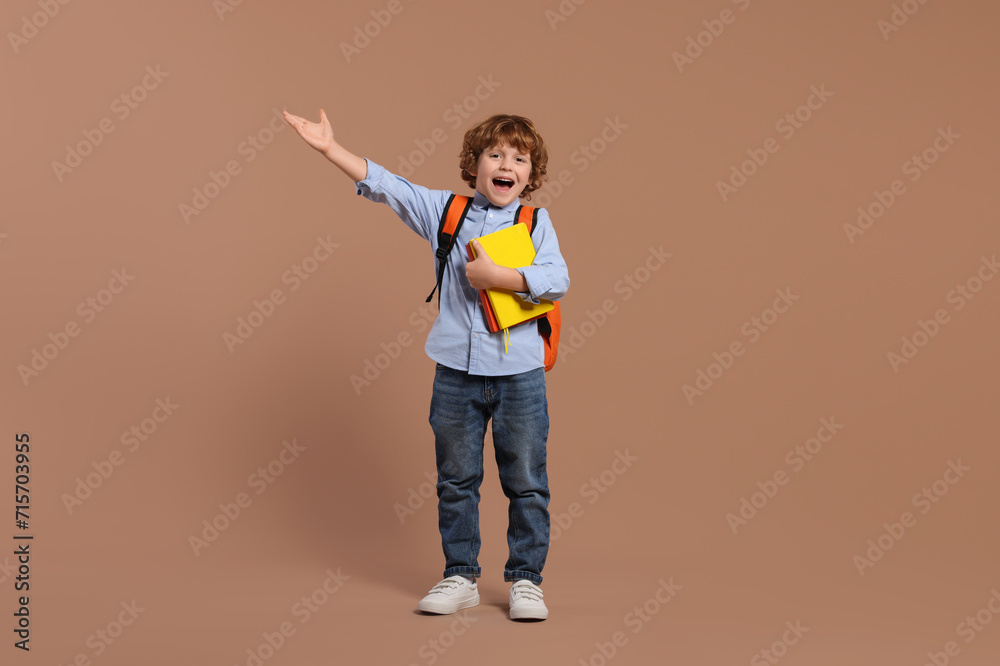Emotional schoolboy with backpack and books on brown background Emotional schoolboy with backpack and books on brown background
