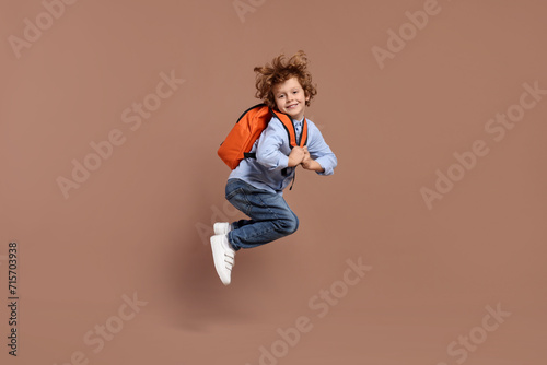 Happy schoolboy with backpack jumping on brown background