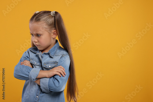 Resentful girl with crossed arms on orange background. Space for text