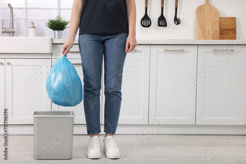 Woman taking garbage bag out of trash bin in kitchen, closeup. Space for text photo
