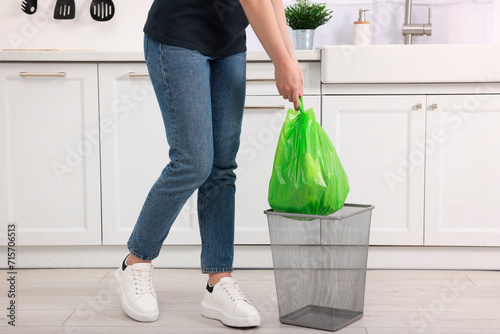 Woman taking garbage bag out of trash bin in kitchen, closeup photo