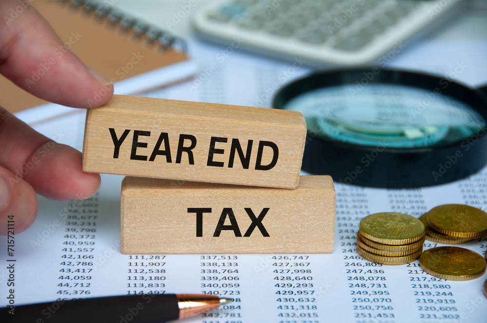 Year end tax text on wooden block with pen, notepad, calculator and coins background. Tax assessment concept - obrazy, fototapety, plakaty 