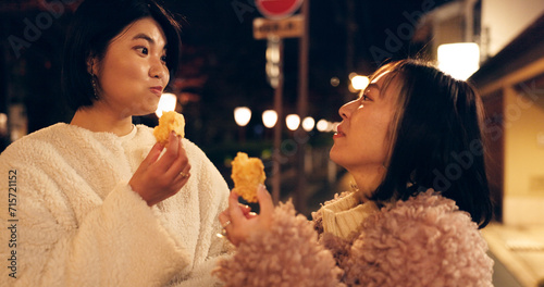 Woman, friends and street food or eating Japanese snack for travel experience, hungry or local trip. Female people, sidewalk and night walk on vacation for nutrition culture, adventure or traditional photo