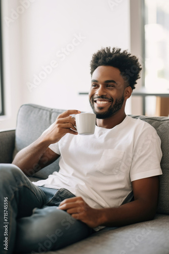 African American man drinking coffee sitting on sofa at home