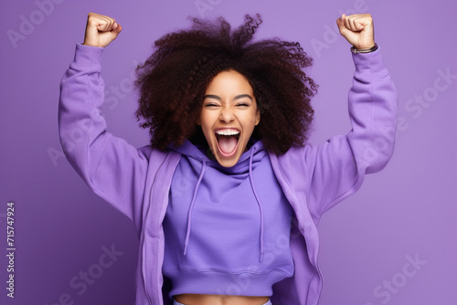 Overjoyed cheerful African American woman dressed stylish clothes celebrate success raise hands fists isolated on purple color background