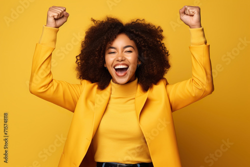 Overjoyed cheerful African American woman dressed stylish clothes celebrate success raise hands fists isolated on yellow color background