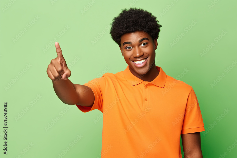 Positive excited African American guy wear orange shirt looking pointing empty space isolated on green color background Positive excited African American guy wear orange shirt looking pointing empty space isolated on green color background