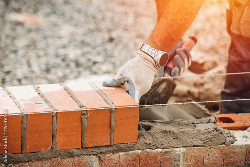 Industrial bricklayer laying bricks on cement mix on construction site close-up photo