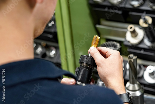 A worker inspects and selects a tap for cutting threads in parts on a CNC milling and turning machine. © andov