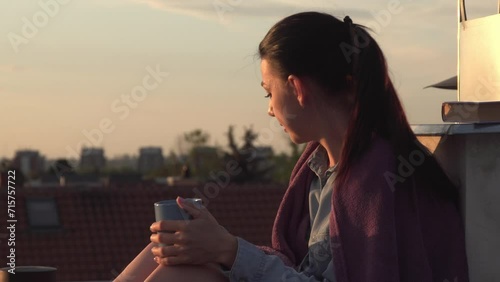A woman sits on a rooftop, delighting in the sunset.  smiles, sipping tea from a mug during a tranquil evening. photo