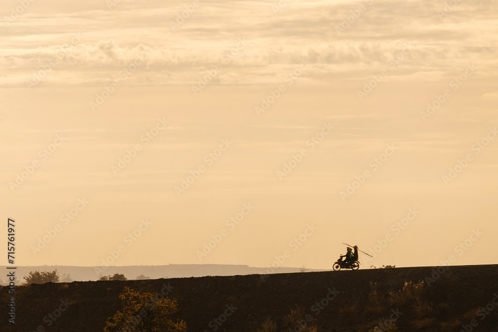 Silhouette of two men biker and a motorcycle on the road with sunset light background