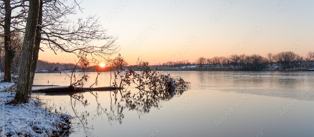 Winter landscape with sunset in the forest next to the frozen lake