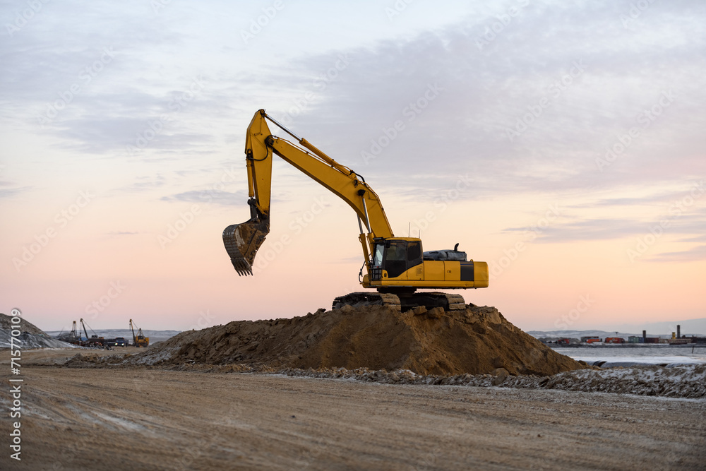 Yellow excavator working on construction site. The road construction. Yellow excavator working on construction site. The road construction.