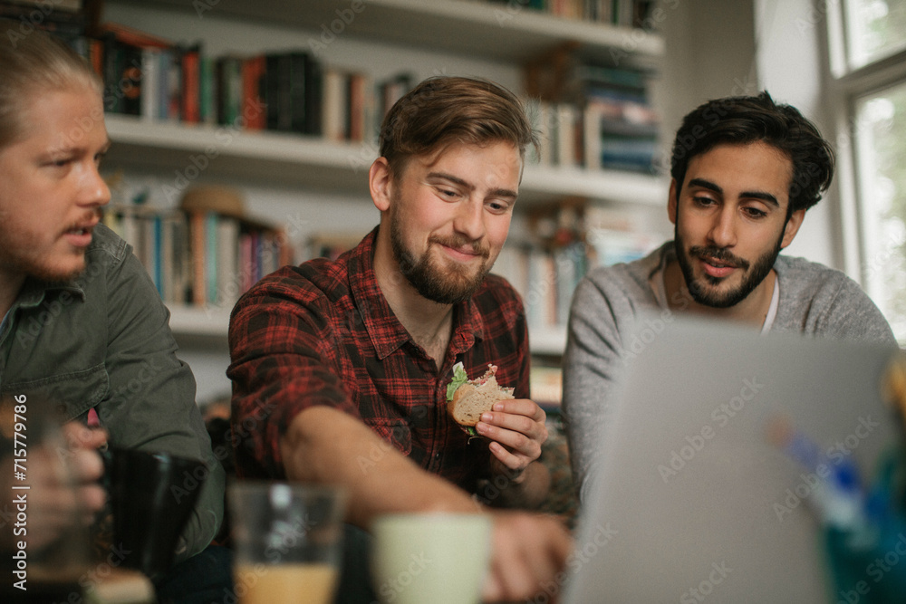 Group of young men working on laptop and eating snacks at home Group of young men working on laptop and eating snacks at home