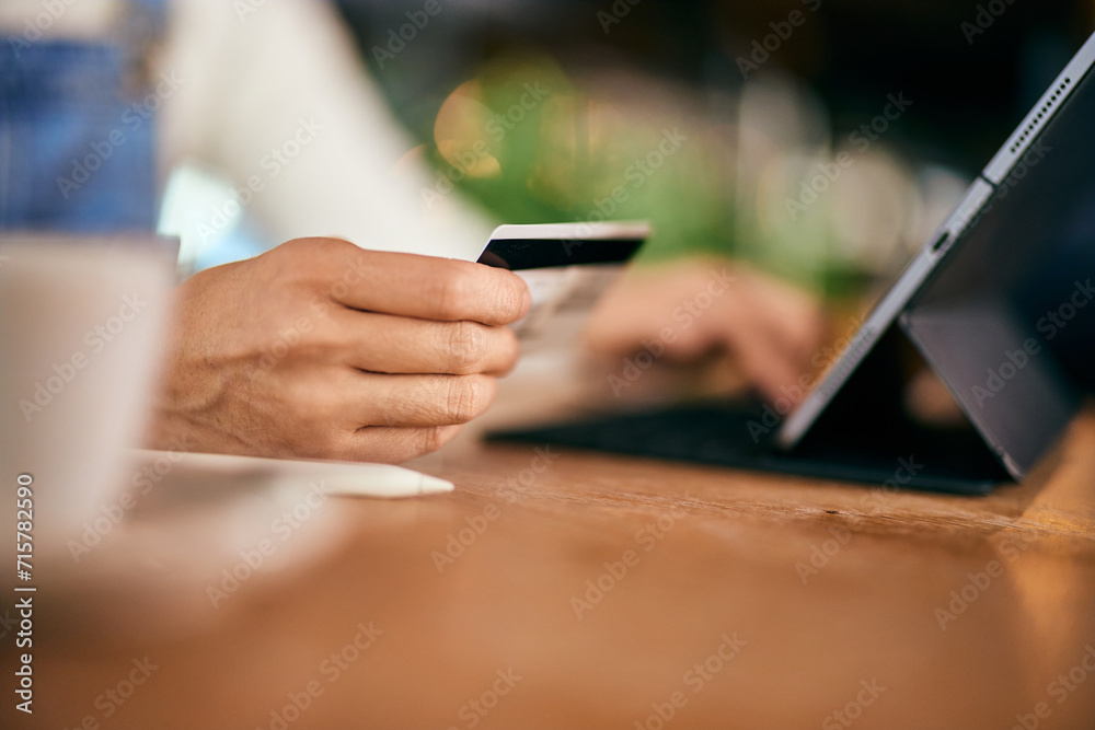A female hand holding a credit card and using a tablet, at the cafe. A female hand holding a credit card and using a tablet, at the cafe.