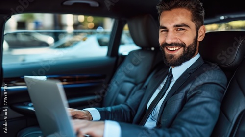 Handsome businessman working on laptop computer while sitting in luxury car. © Oulaphone