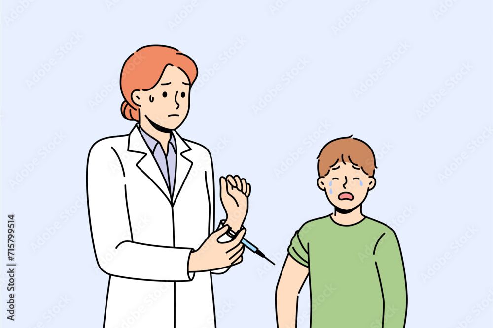 Boy suffers vaccine phobia and is crying standing near woman doctor holding syringe with injection in hands. Nurse hesitates to inject vaccine into young patient who is throwing tantrum. Boy suffers vaccine phobia and is crying standing near woman doctor holding syringe with injection in hands. Nurse hesitates to inject vaccine into young patient who is throwing tantrum.