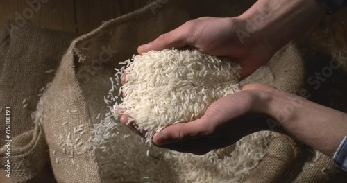Super slow motion close up of farmer is controlling quality of handful dry basmati quality white rice over burlap sack background at 1000 fps. photo