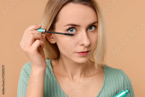Beautiful woman applying mascara on beige background, closeup