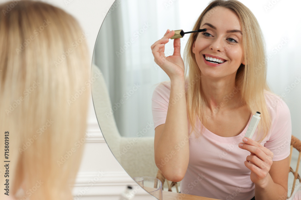 Beautiful woman applying mascara near mirror at home Beautiful woman applying mascara near mirror at home