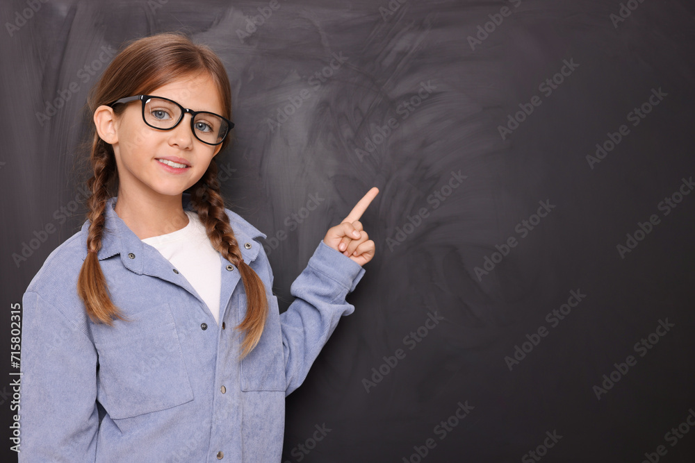 Smiling schoolgirl in glasses pointing at something on blackboard. Space for text Smiling schoolgirl in glasses pointing at something on blackboard. Space for text