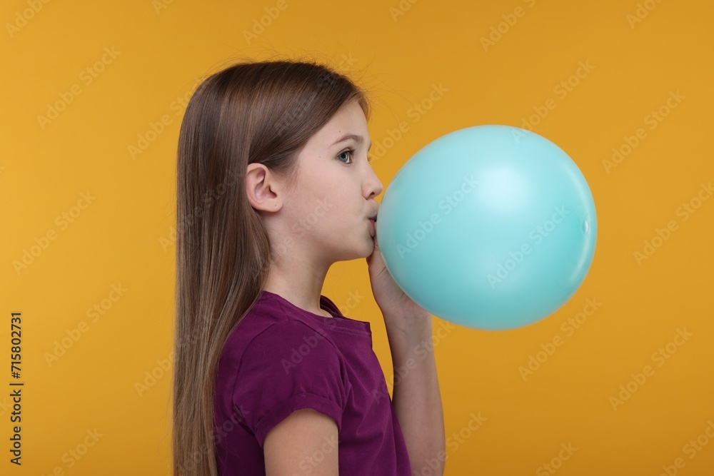 Girl inflating bright balloon on orange background Girl inflating bright balloon on orange background