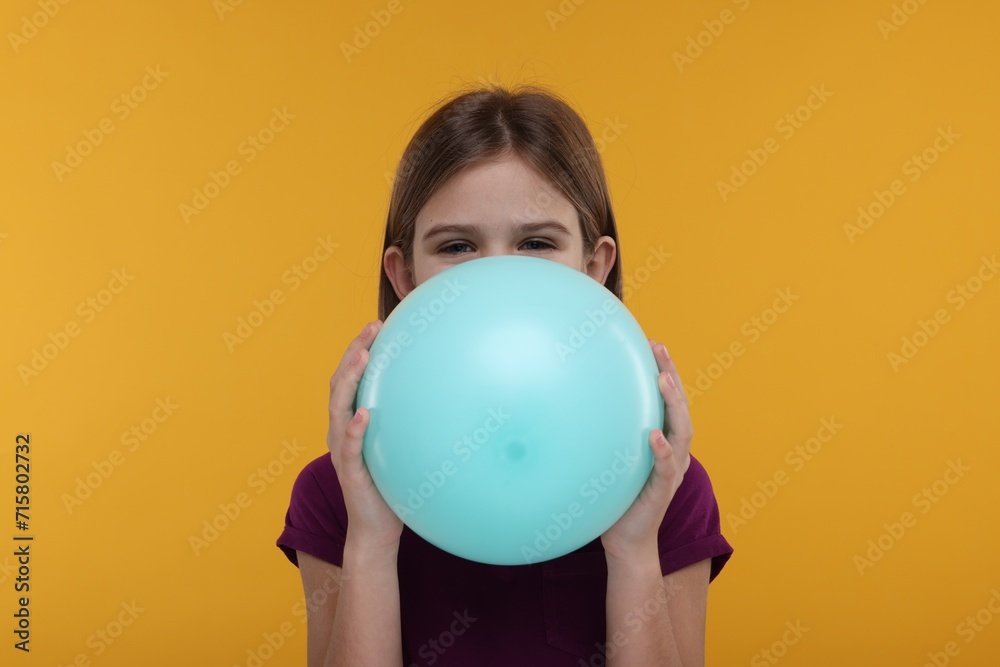 Girl inflating bright balloon on orange background Girl inflating bright balloon on orange background