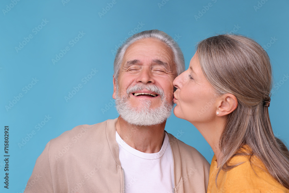 Senior woman kissing her beloved man on light blue background, space for text