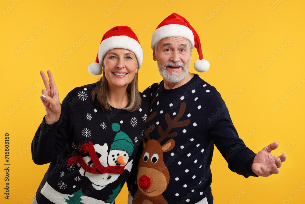 Happy senior couple in Christmas sweaters and Santa hats on orange background Happy senior couple in Christmas sweaters and Santa hats on orange background