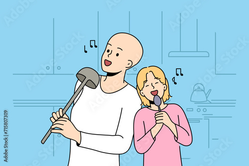 Hairless boy and little girl sing standing in kitchen, use utensils instead microphone, imagine visit in karaoke. Sister supports brother dreams of going to karaoke after undergoing cancer treatment