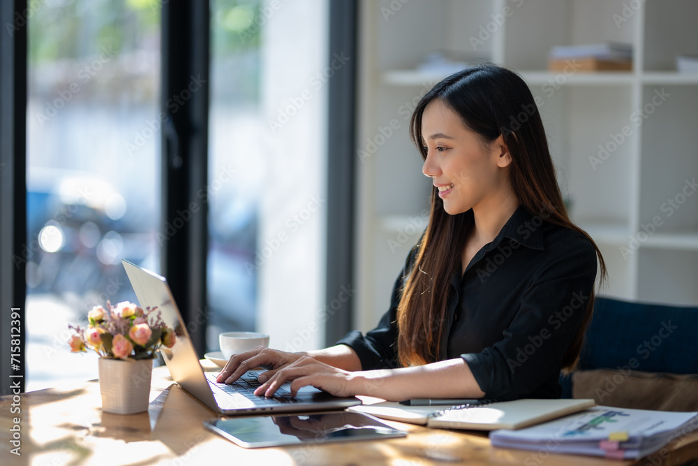 Freelance Asian woman working happily on laptop in the morning with sunlight shining through the glass on the table. Freelance Asian woman working happily on laptop in the morning with sunlight shining through the glass on the table.