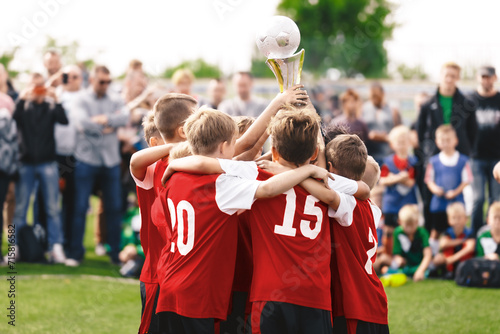 Happy children winning sports tournament. Kids in sports teams win trophies on tournaments Schoolboys standing in a circle and holding the golden trophy. Victory celebration of a youth sports team photo