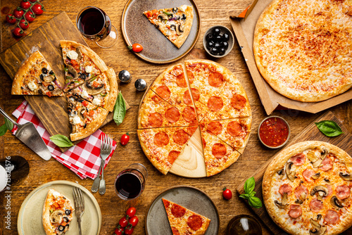 Family or friends pizza party. Flat-lay of different types of pizza and red wine over rustic wooden table, top view. photo
