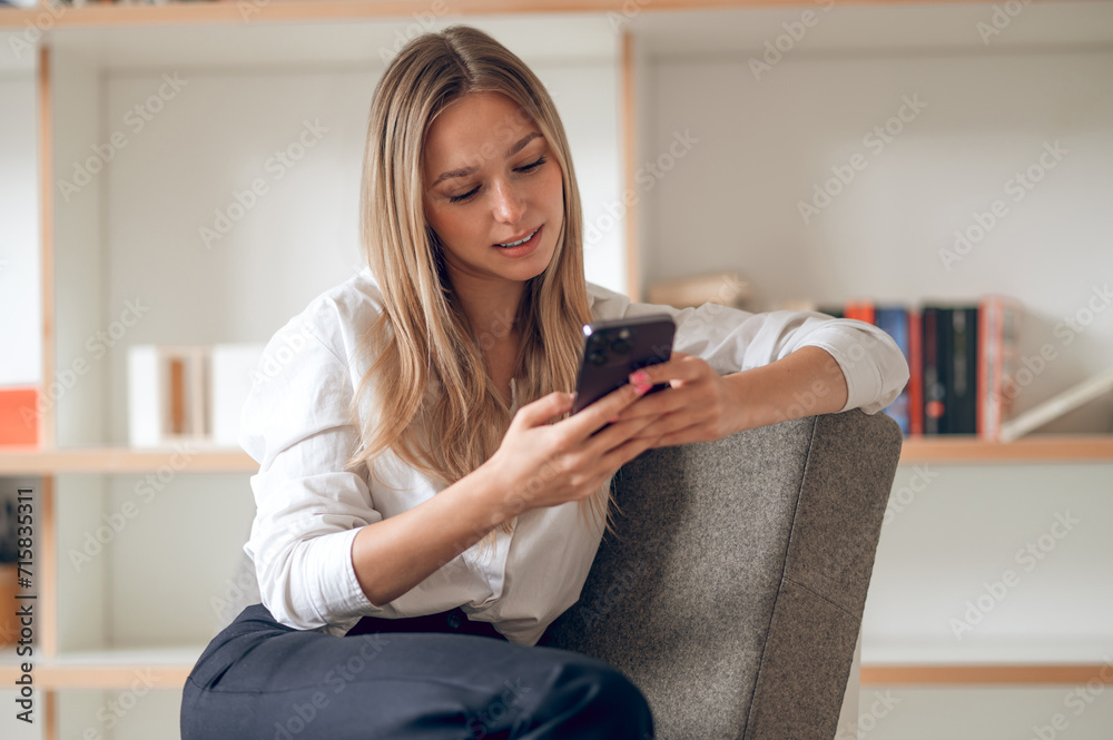 Happy woman in white shirt using cellphone while sitting in her appartement. Happy woman in white shirt using cellphone while sitting in her appartement.