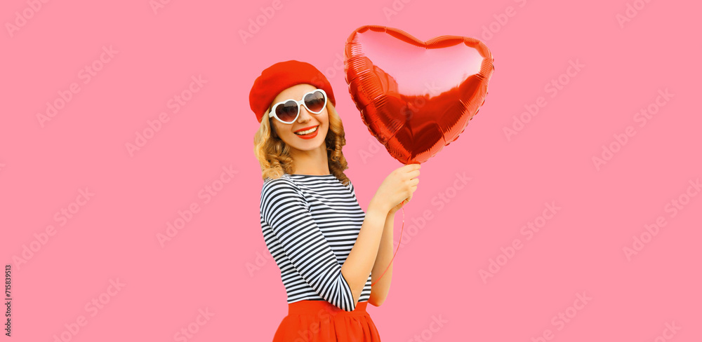 Portrait of happy cheerful smiling woman with red heart shaped balloon wearing french beret on pink background - obrazy, fototapety, plakaty 