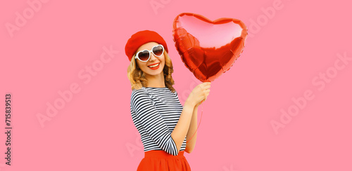Portrait of happy cheerful smiling woman with red heart shaped balloon wearing french beret on pink background