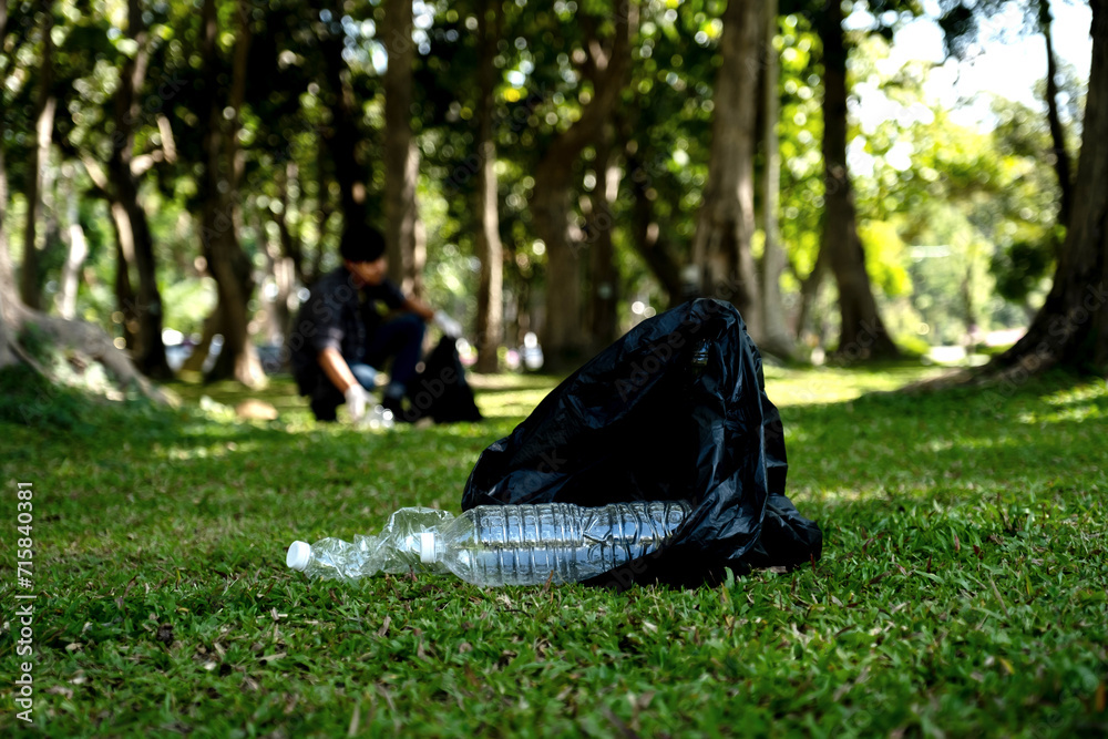 plastic bottle waste, man picking up trash and putting it in the black garbage bag at the Park on Environmental Earth day plastic bottle waste, man picking up trash and putting it in the black garbage bag at the Park on Environmental Earth day