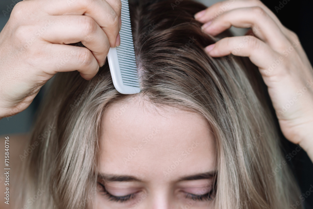 Fototapeta premium Cropped shot of a young blonde woman parting her hair using a thin comb. Hair styling. Сoloring the overgrown roots of the head