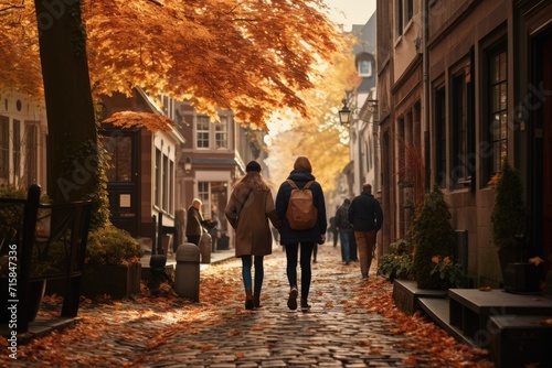 Two people walk through a cobblestone street lined with historic buildings, as autumn leaves blanket the ground in a quaint town