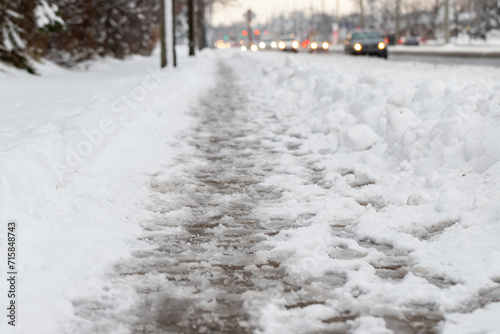 Winter road with melting from salt snow. Close up of sidewalk with slush on snowy day © Iryna
