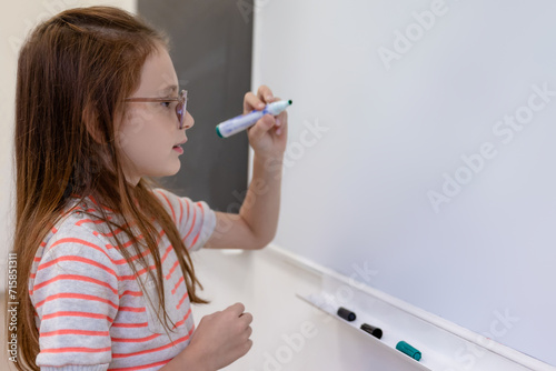 Pupil girl doing mathematics task on while board during lesson.