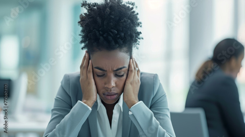 Stressed businesswoman is holding her head in her hands at her desk, showing signs of frustration or headache in an office environment. photo