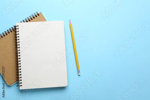 Notebooks and pencil on light blue background, top view. Space for text
